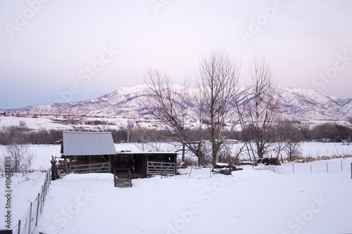 old barn outside in the snow country scene with mountains in background