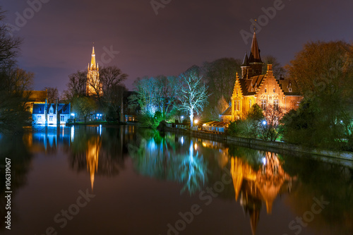 Fairytale night landscape with Church of Our Lady and medieval house on Lake Minnewater in Bruges, Belgium