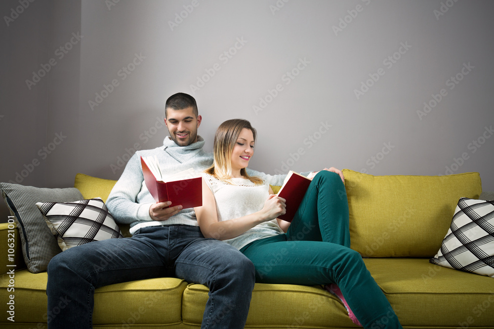 Young woman and man reading a book together. They are sitting on the sofa. Young woman and man reading a book together. They are sitting on the sofa.