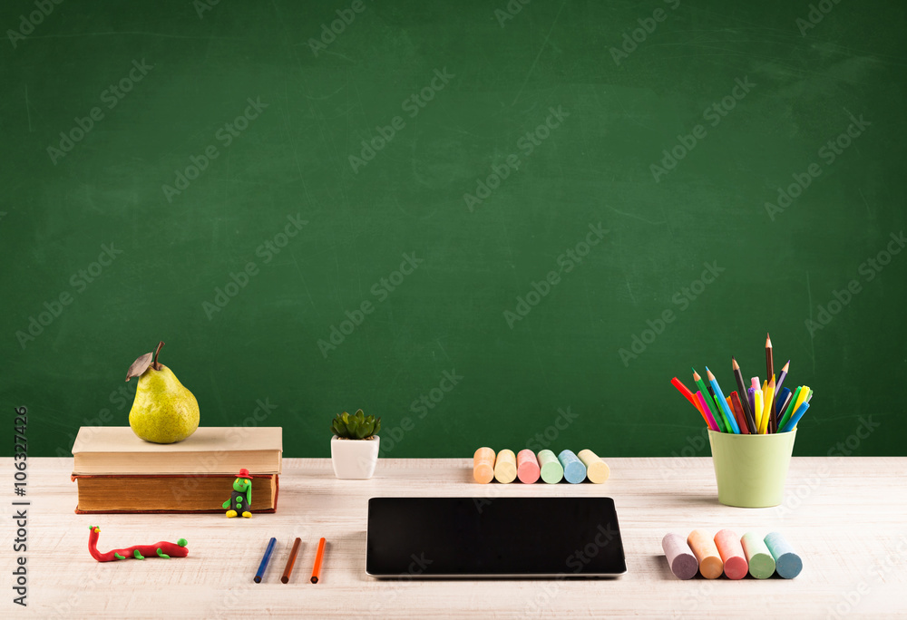 School items on desk with empty chalkboard School items on desk with empty chalkboard