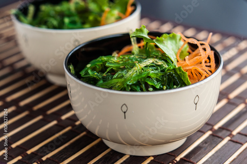 Two bowls of Japanese Chuka Wakame seaweed salad on bamboo mat, close-up photo