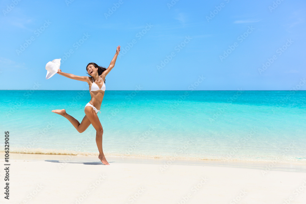 Happy bikini woman jumping of joy and success on perfect white sand beach on caribbean tropical vacation. Holiday girl with sexy slim suntan body running of freedom and happiness.