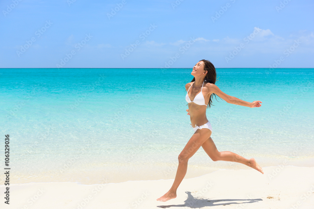 Beach bikini woman carefree running in freedom fun. Joyful happy Asian girl relaxing showing joy and happiness in slim body for weight loss diet concept on perfect white sand.