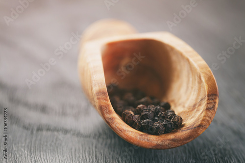 black pepper in olive scoop on wood table, vintage toned