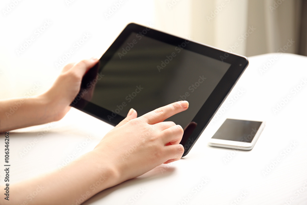 Mobile phone and female hands using modern tablet, indoors Mobile phone and female hands using modern tablet, indoors