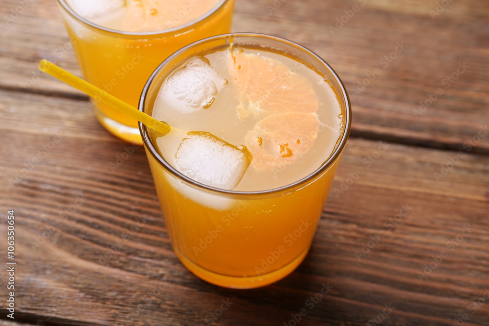 Glasses of orange juice with ice blocks and tubule on wooden background Glasses of orange juice with ice blocks and tubule on wooden background