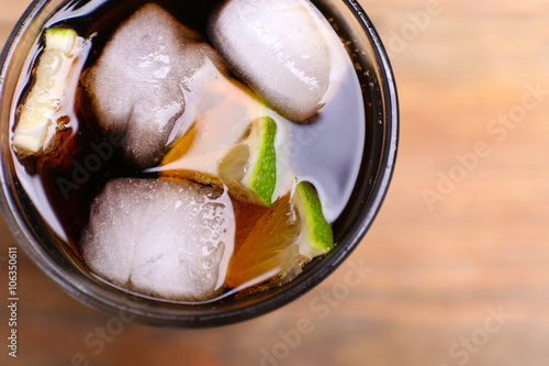 Cocktail with lime slices and ice blocks on wooden table, close up