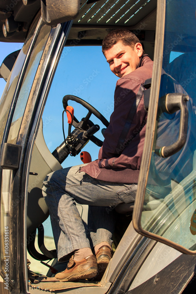 smiling young man sits in cab of tractor