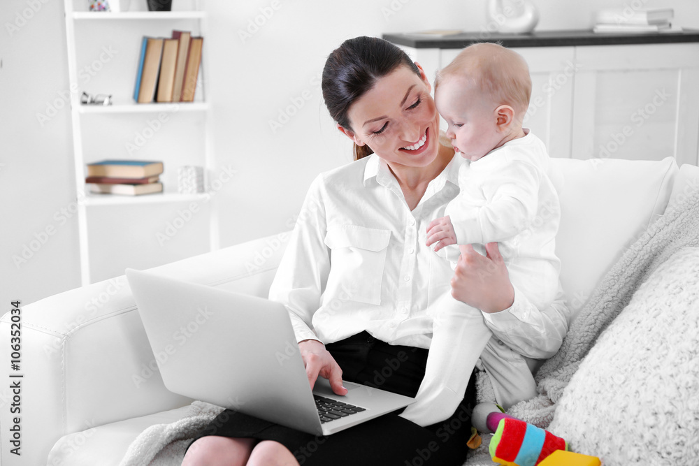 Businesswoman with baby boy on couch working from home using laptop Businesswoman with baby boy on couch working from home using laptop