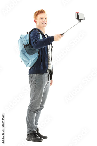 Young handsome boy with backpack using stick for photo by his self, isolated on white