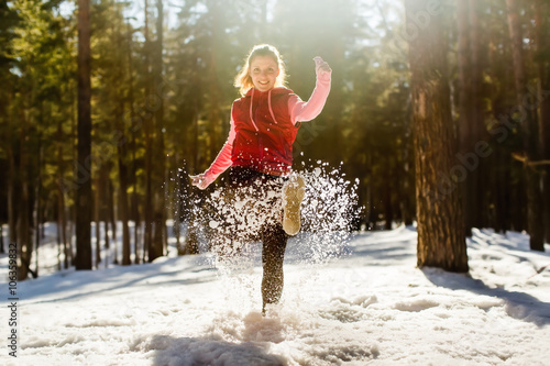 Happy girl kicking snow on beautiful winter day.