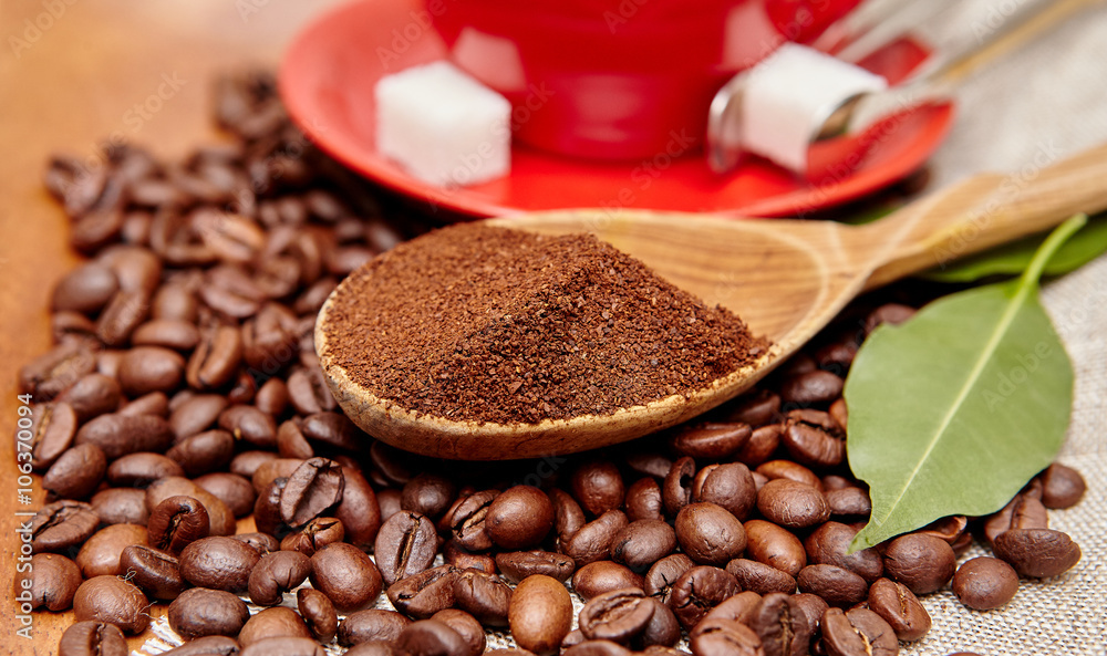 Fototapeta premium Natural ground coffee heap in a wooden spoon on a background of coffee beans and red cup