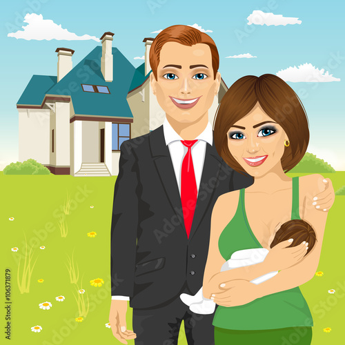 husband in a business suit standing next to his wife breastfeeding in front of classic cottage