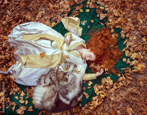 A fairytale fantasy. Red-headed woman in autumn forest. She dressed in renaissance costume. With dog