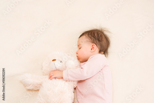 Amazing portrait of sleeping beautiful baby toddler girl with a fluffy teddy bear on the bed