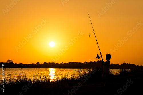 little boy fishing in the river sunset background