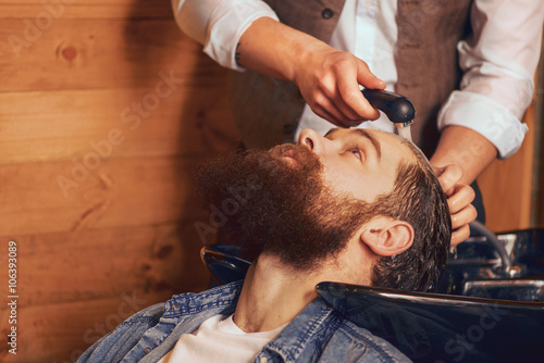 Barber washing head of bearded man