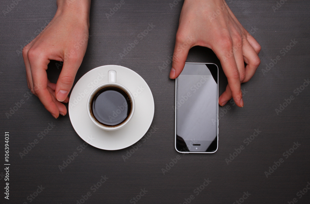 Fototapeta premium Woman hands touching smart phone and holding coffee cup. Top view