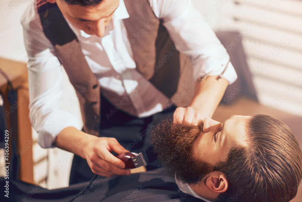 Fototapeta premium Professional barber cutting beard of pleasant man