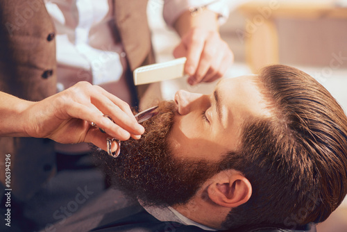 Fotografie Professional barber cutting beard of handsome man