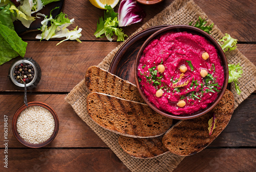 Roasted Beet Hummus with toast in a ceramic bowl on a wooden background. Top view