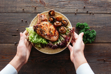 Waiter serving a chicken dish with lettuce and mushrooms. Chief decorating food for presentation in small cafe. Waiter presenting grilled chicken with salad for retail. 