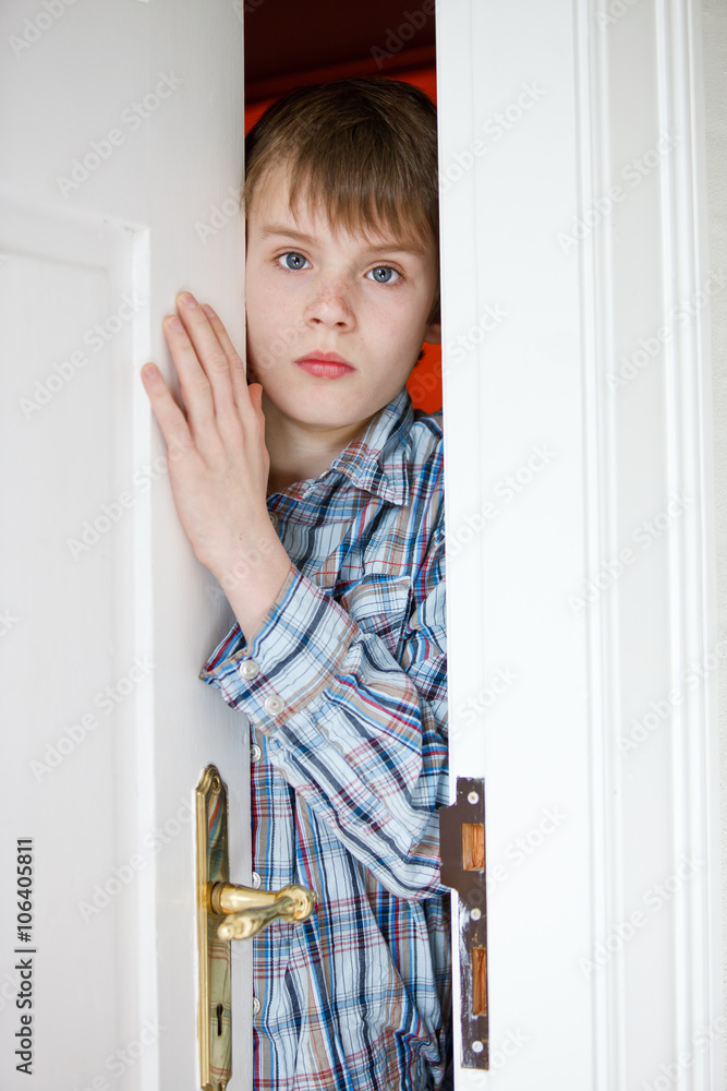 Young boy peering through a partially opened door Young boy peering through a partially opened door