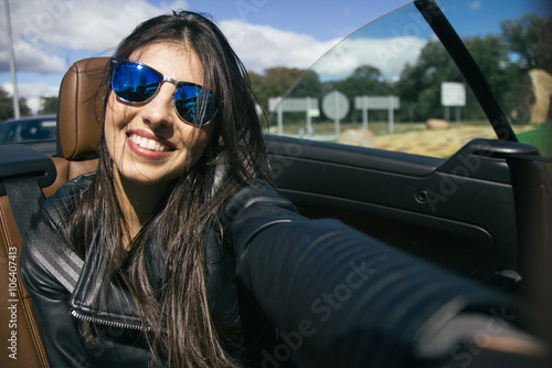 Beautiful woman with sunglasses taking a selfie photo in a convertible car © aglphotography