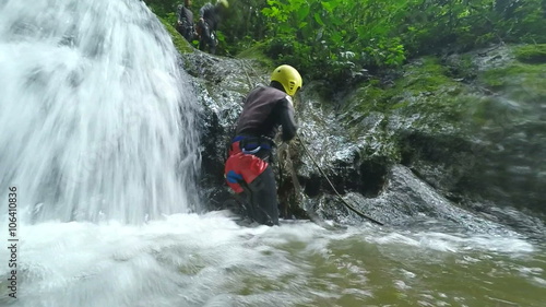 Experience the thrill with slow motion footage of Asiatic men tourists engaging in exhilarating waterfall rappelling adventure.