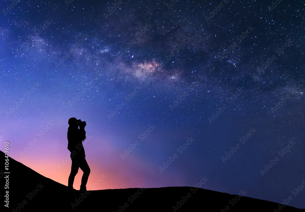 Silhouette of woman is taking the milky way photo on top of mountain before sunrise.
