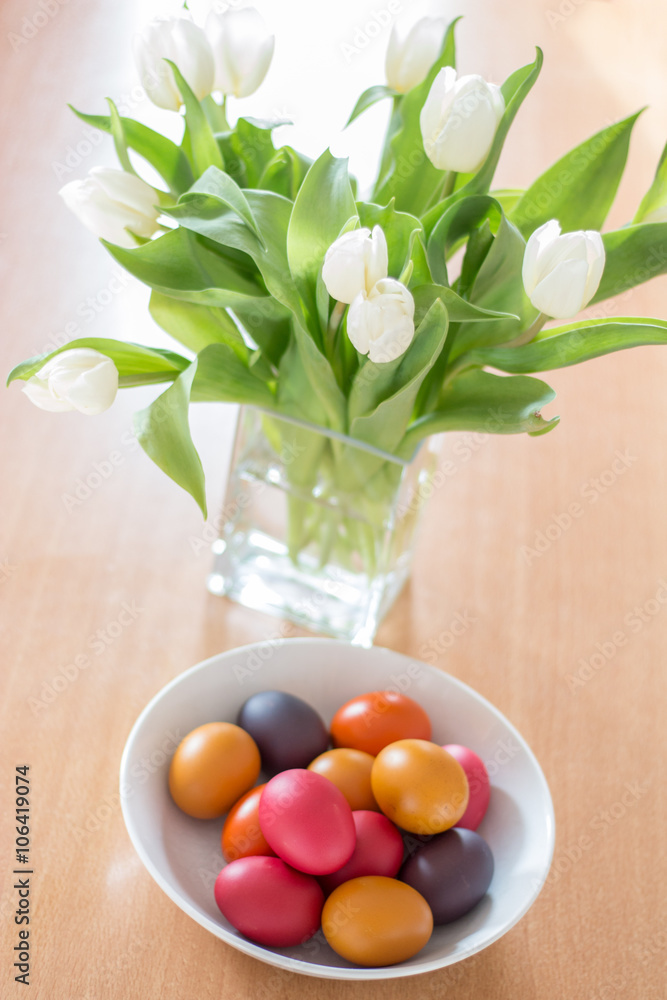Schüssel mit Ostereiern und Strauß weißer Tulpen