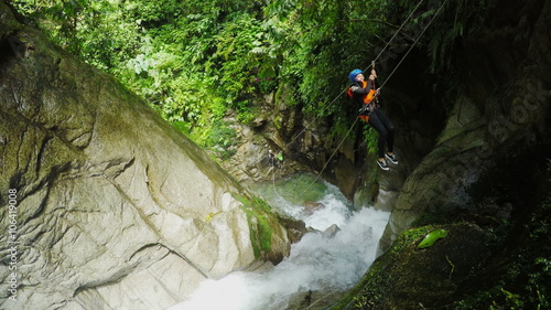 Experience the thrill of canyoning as a brave tourist woman captures every exhilarating moment on an action camera,including a breathtaking zipline ride over a majestic waterfall.