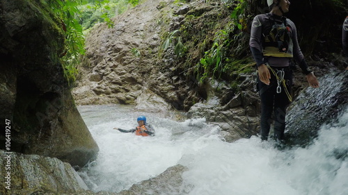 Experience the thrill of canyoning as young women are guided through a waterfall by their tour leader,captured in dynamic static camera footage with immersive sound.