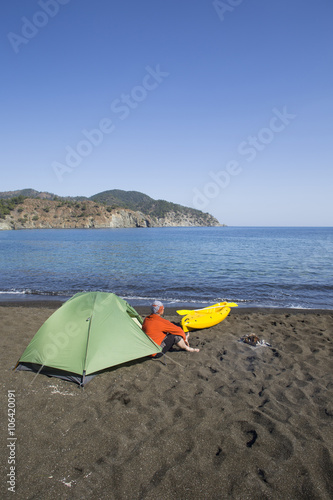 A man sits in a tent camp on the beach.