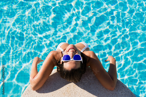 Top view of funny woman enjoying summer vacation in resort swimming pool. Beautiful brunette girl wearing sunglasses and having fun on summertime.
