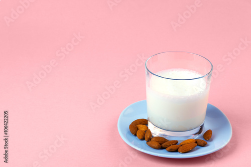 Glass of almond milk on a pale blue plate on a pink surface