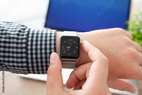 man hand holding smart Watch on the background of notebook