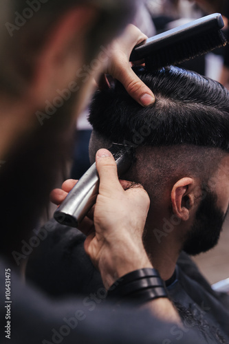 Male barber combing and shaving hair of a male client