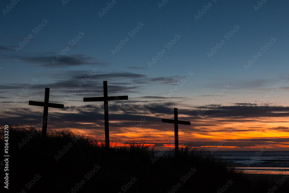 Three crosses on a sand dune with a sunset over the sea.
