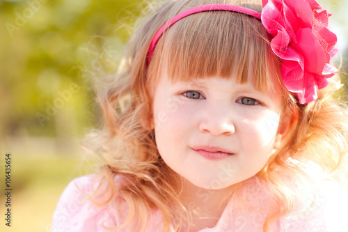 Smiling kid girl 3-4 year old wearing floral hairband outdoors. Looking at camera. Childhood.