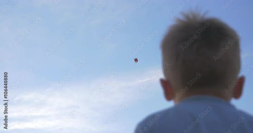 Low-angle shot of a boy waving hand to sky lantern flying high in the air. Low-angle shot of a boy waving hand to sky lantern flying high in the air.