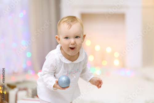 Funny baby girl with Christmas toy near  Christmas tree on bright background
