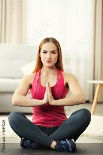Young sportswoman sitting in lotus position on a mat at home