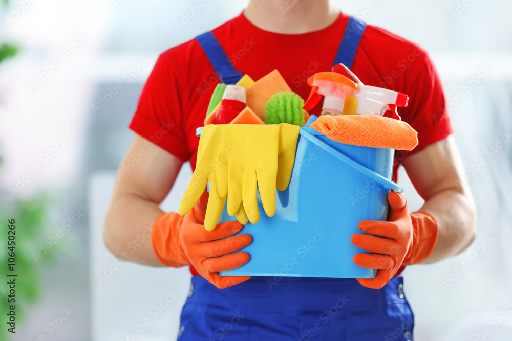 Young janitor holding cleaning products and tools on bucket, close up Young janitor holding cleaning products and tools on bucket, close up
