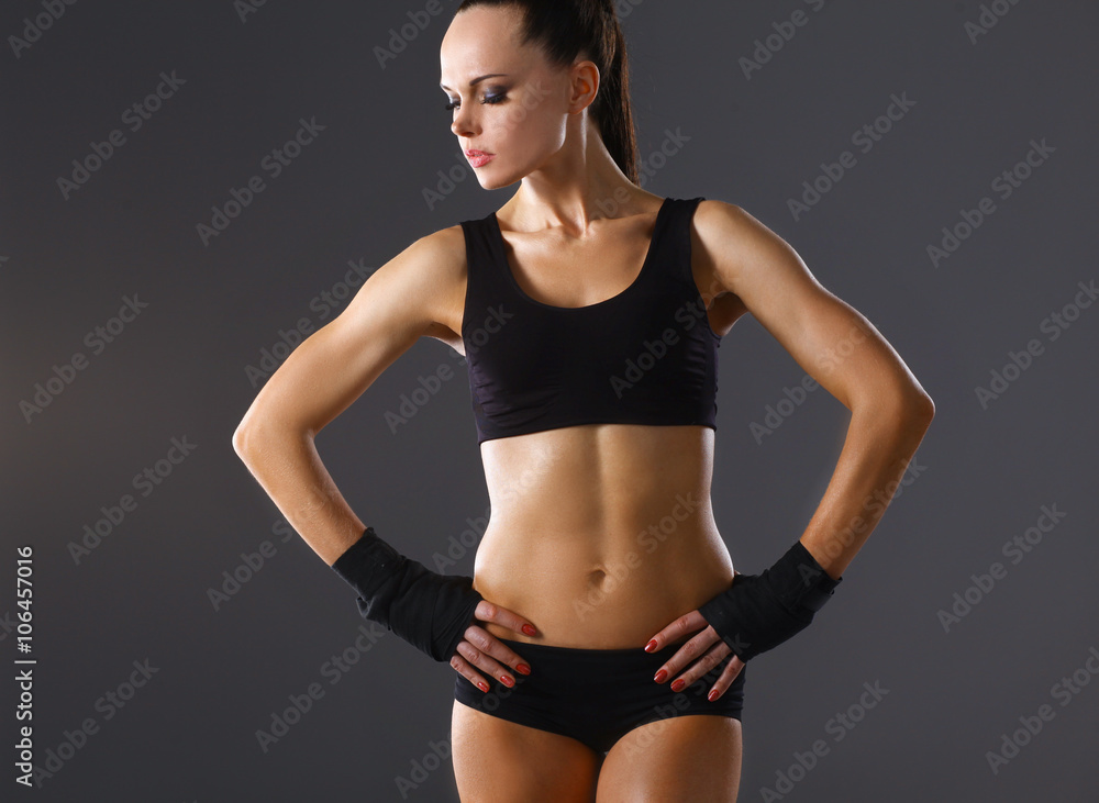 Muscular young woman standing on gray background Muscular young woman standing on gray background