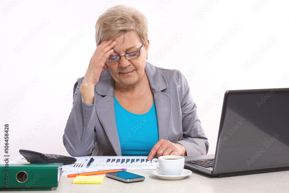 Elderly business woman holding hand on her head and working at her desk in office, business concept Elderly business woman holding hand on her head and working at her desk in office, business concept
