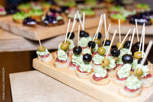 Wooden tray of appetizers on pallet coffee table at banquet with jamon, butter cream and olives. Selective focus.