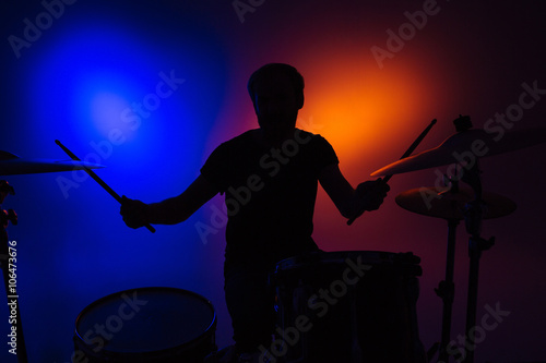 Silhouette of man drummer sitting and playing drums with sticks