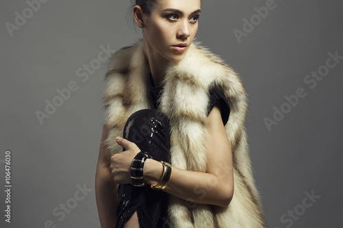Sexy Beauty Girl with natural  Make up.  Fashion Brunette Portrait of a girl dressed in fur coat and black shirt posing on a grey background. Retro style