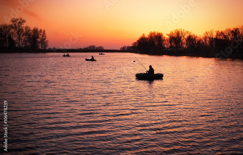Beautiful landscape with orange sunrise, lake and fishermen 